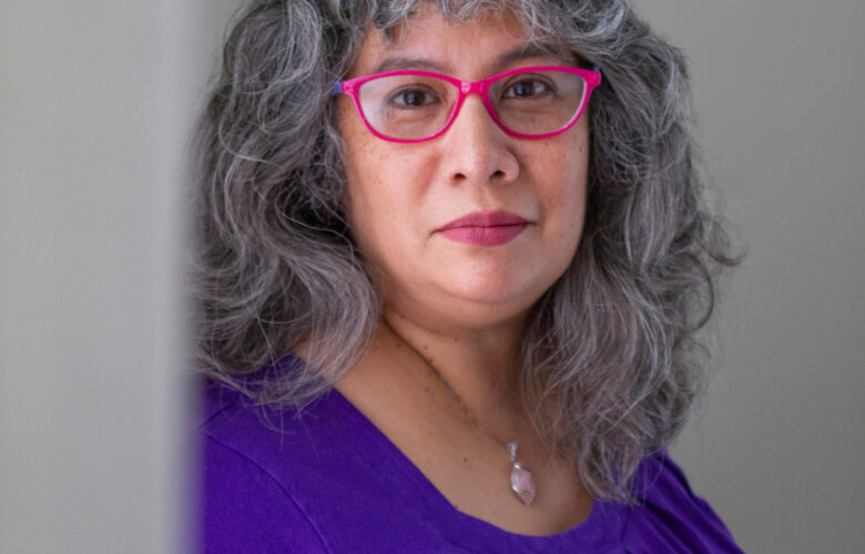 Middle-aged woman with long, dark gray hair and glasses gazes into camera