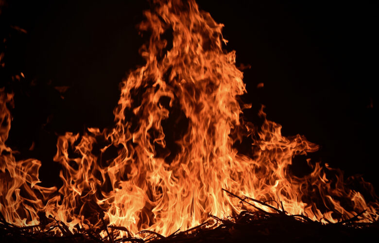Trash fire in darkness with orange flames climbing up the entire photo