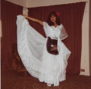 Mexican American woman in a white dress with a sheer outer layer and black apron, the traditional folklorico costume for the Veracruz region of Mexico.