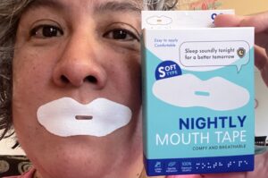 Mouth covered with white lip-shaped tape with slit in the middle and box that says "Nightly Mouth Tape."